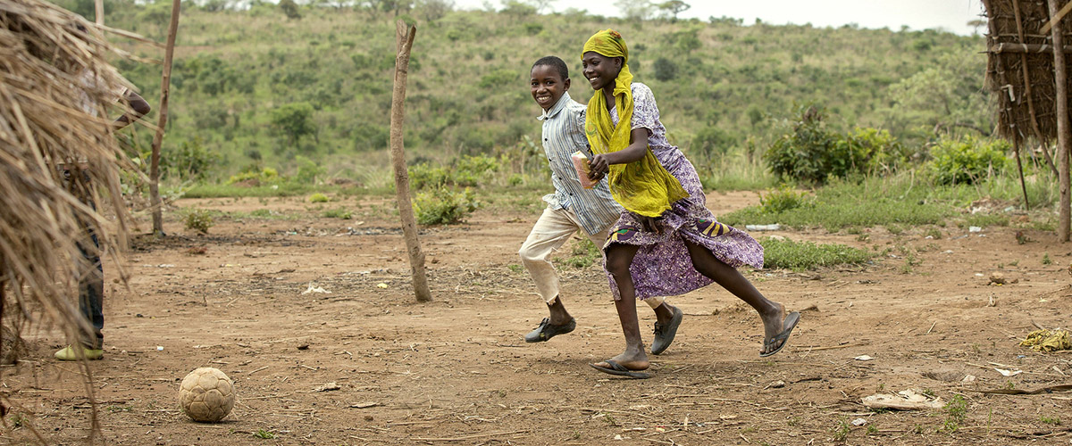 Salamatou, 12, steps out from work at her mother's restaurant to cut herself slices of mango as a snack. She sees a group of boys nearby playing football and immediately runs to join them. Photo: UN Women/Ryan Brown