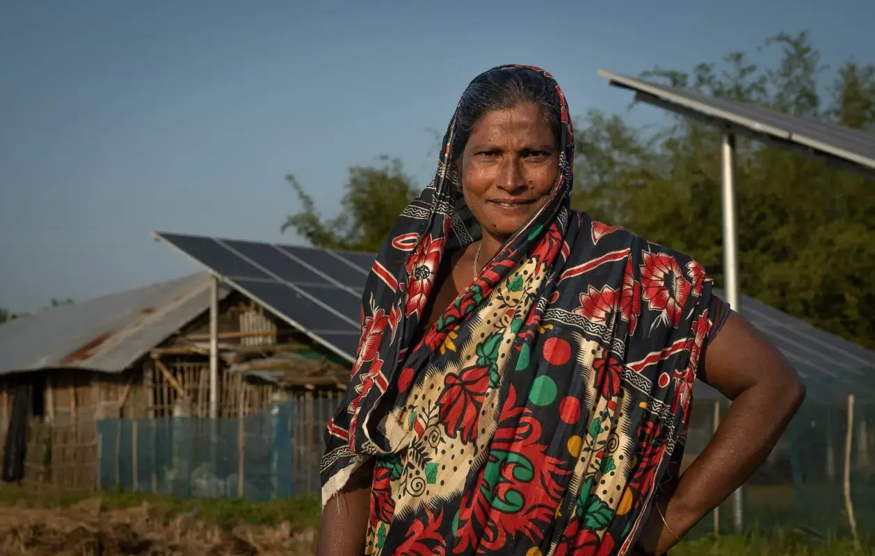 A woman poses in front of the solar panels helping to power her farm